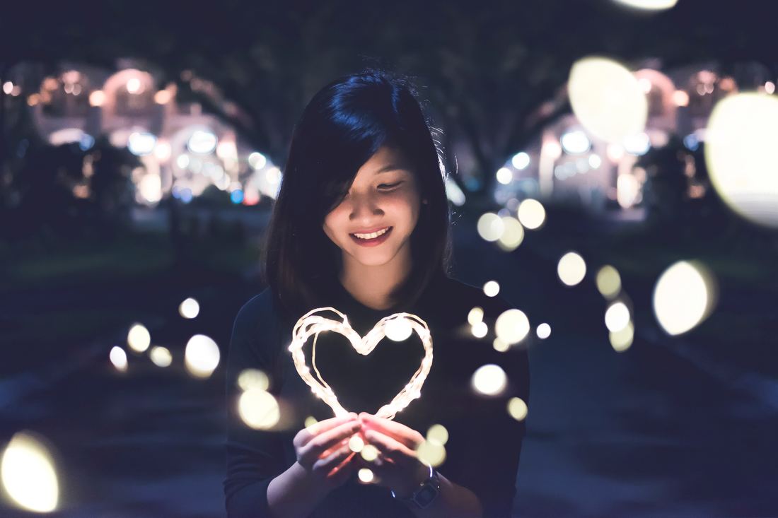 A girl holding a neon heart in the dark, sharing her personal self-discovery