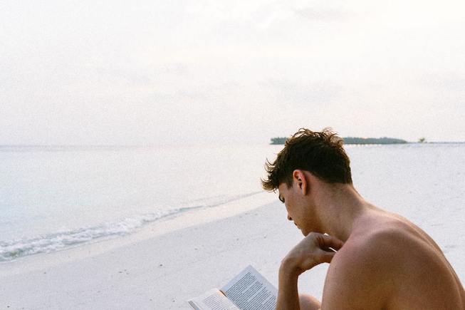 A man on a beach reading a book recommended by the Work In Progress book club