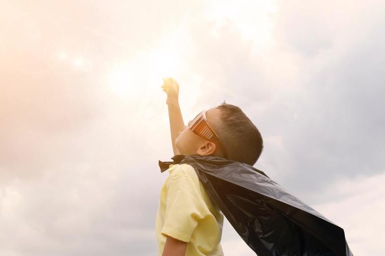 A boy dressed as a superhero reaching for the sky towards his goals