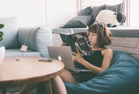 A girl sitting in a beanbag reading a career coaching self-help book with a laptop in her lap