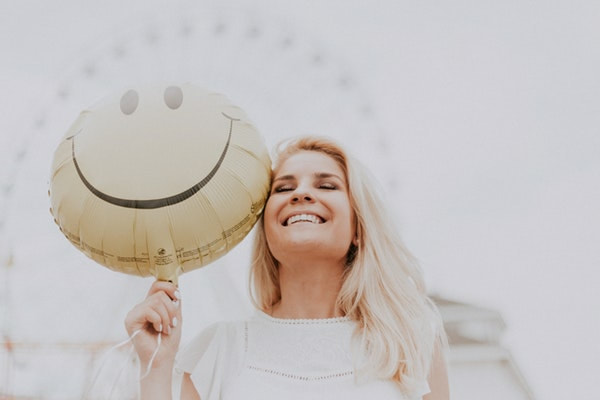 A confident woman holding a smiley face balloon